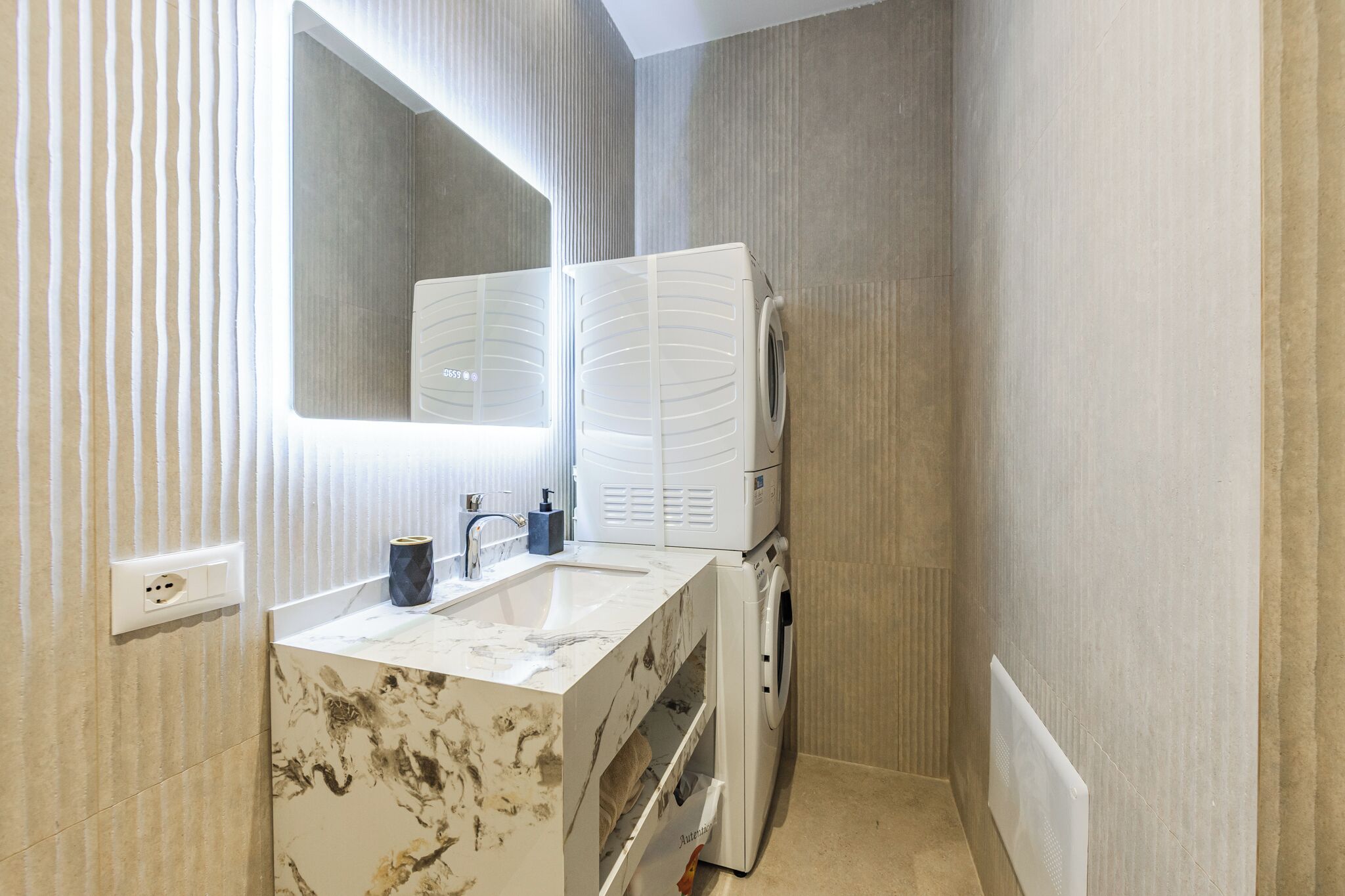 A bathroom with a marble sink, a mirror, a built-in heater, and a washing machine.