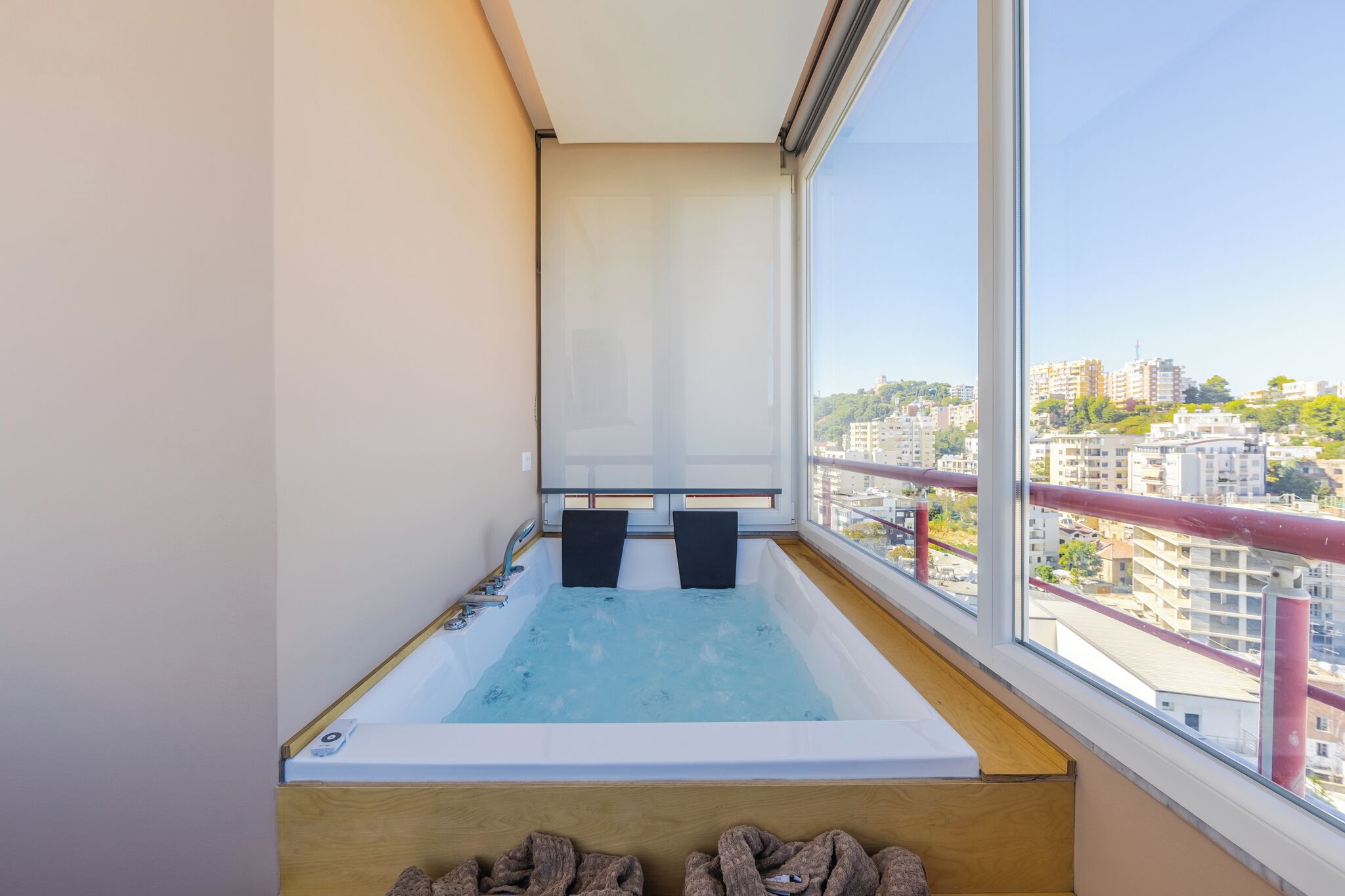 A modern bathroom with a large bathtub, two black towels, and a view of a cityscape through a large window.