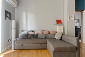 Ein modernes Wohnzimmer mit einem grauen Ecksofa, einem Heizkörper und einem roten Buch auf einem Regal.