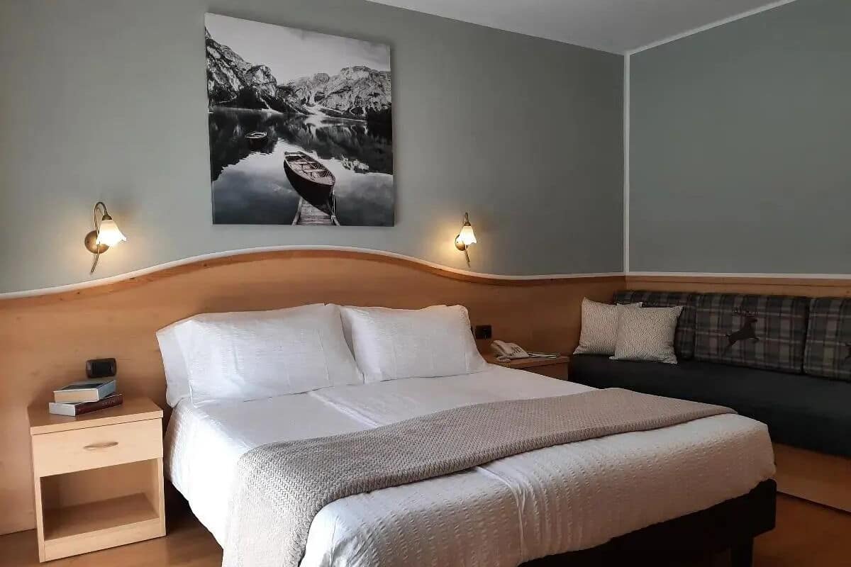 Een slaapkamer met een groot bed, een nachtkastje, een wandlamp, een bank en een schilderij van een berglandschap.