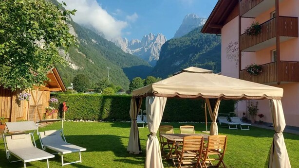 A patio with a table and chairs, a wooden fence, and a mountain view. - Hotel Garnì Arnica (Molveno)