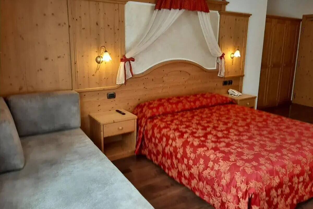 Een slaapkamer met een houten hoofdbord, een rood bloemenbedover, een grijze bank en twee bedlampjes.