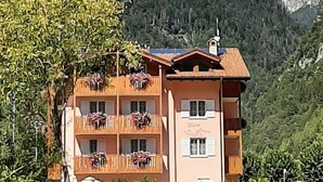 A multi-story building with balconies, set against a mountainous backdrop. - Hotel Garnì Arnica (Molveno)