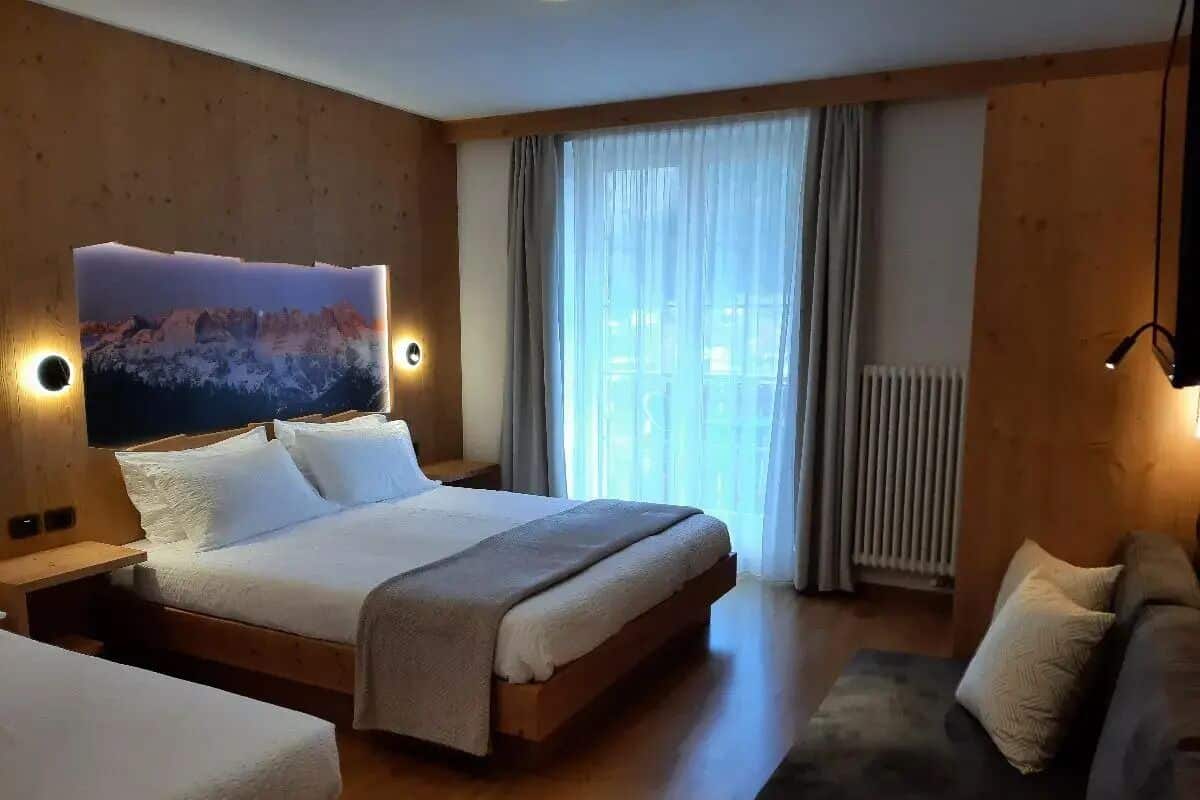 Een hotelkamer met een groot bed, een slaapbank, een aan de muur bevestigde televisie en een raam met gordijnen.