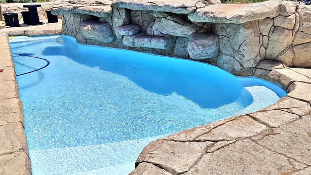 A swimming pool with a rocky edge and a built-in seating area. - WAVES ocean front King Shaka Airport (Desainager)