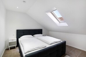 A bedroom with a sloped ceiling, a skylight, a bed with white bedding, a nightstand, and a dark headboard.
