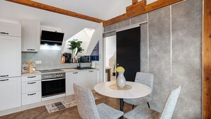 Une cuisine moderne avec des armoires blanches, un four encastré et un coin repas comprenant une table ronde et des chaises.