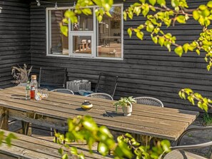 Een houten tuintafel met stoelen, een bloempot en een raam met decoratieve spullen.