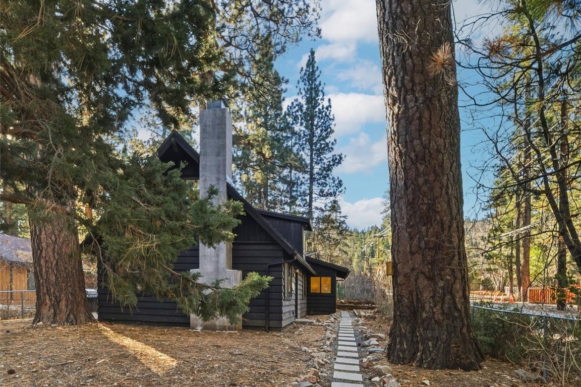 A cabin with a chimney, surrounded by trees and a stone pathway.