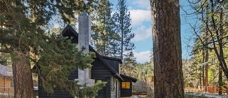 A cabin with a chimney, surrounded by trees and a stone pathway.