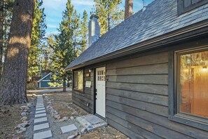 A wooden cabin with a stone pathway leading to the door, surrounded by trees. - PET FRIENDLY 🐾! Foosball! Two Living Rooms! Modern Living! (Big Bear Lake)