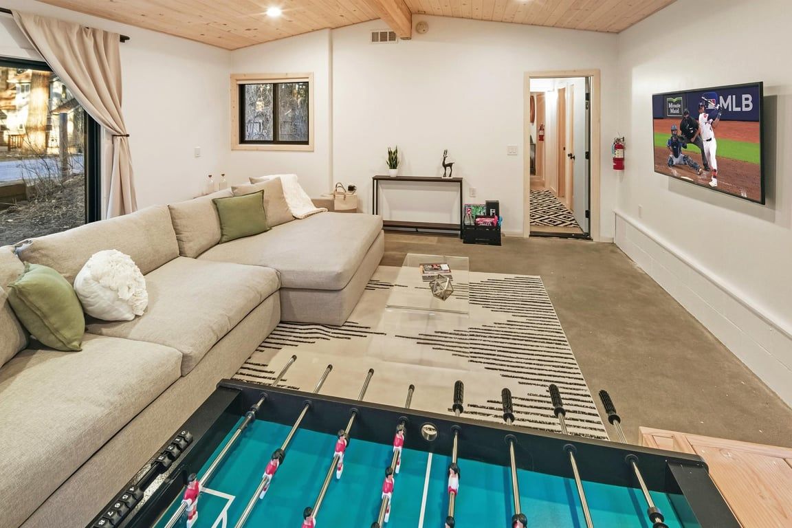 A living room with a foosball table, a sofa, a fireplace, and a television displaying MLB.