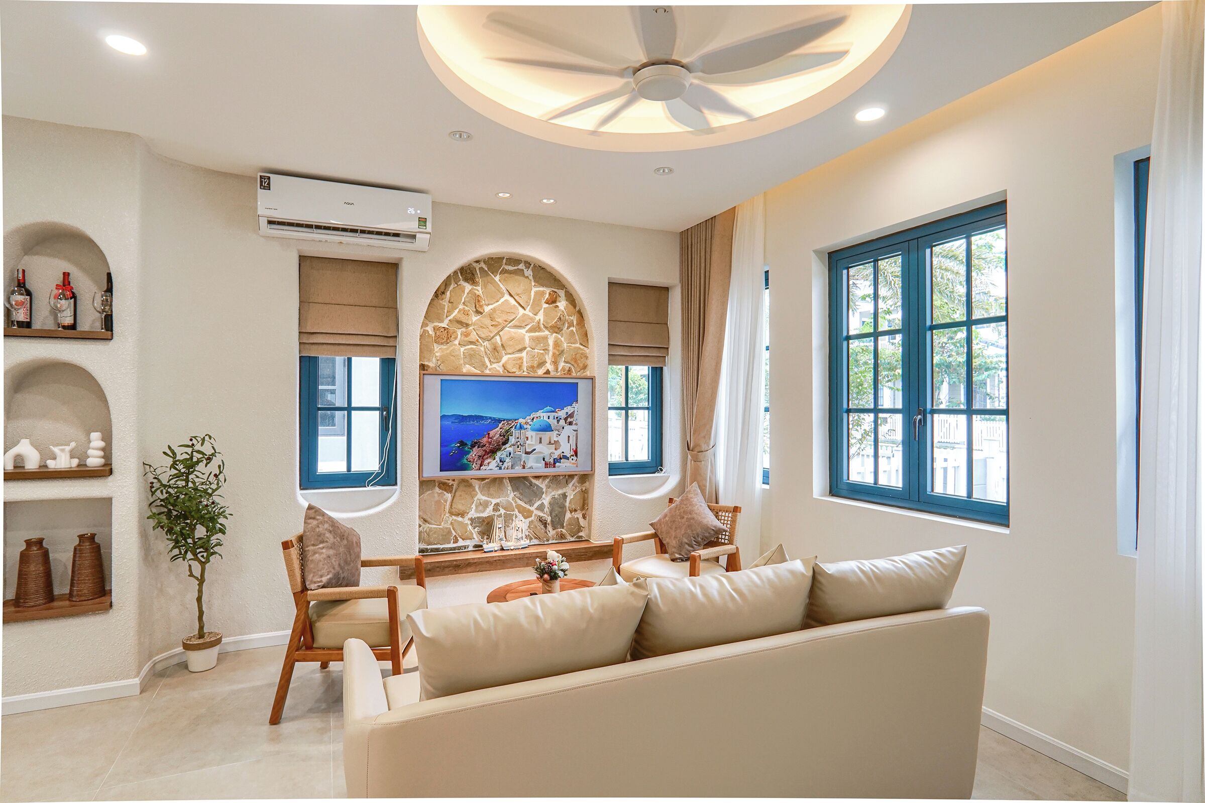 A modern living room with a stone wall, a flat-screen TV, a ceiling fan, and a large window with blue shutters.