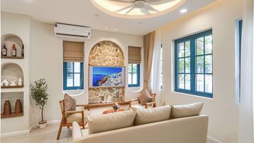 A modern living room with a stone wall, a flat-screen TV, a ceiling fan, and a large window with blue shutters.