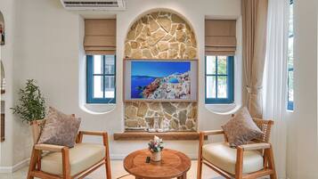 Una habitación con dos sillas de madera, una mesa redonda de madera, una pared de piedra, un televisor montado y una ventana con vistas al paisaje costero.