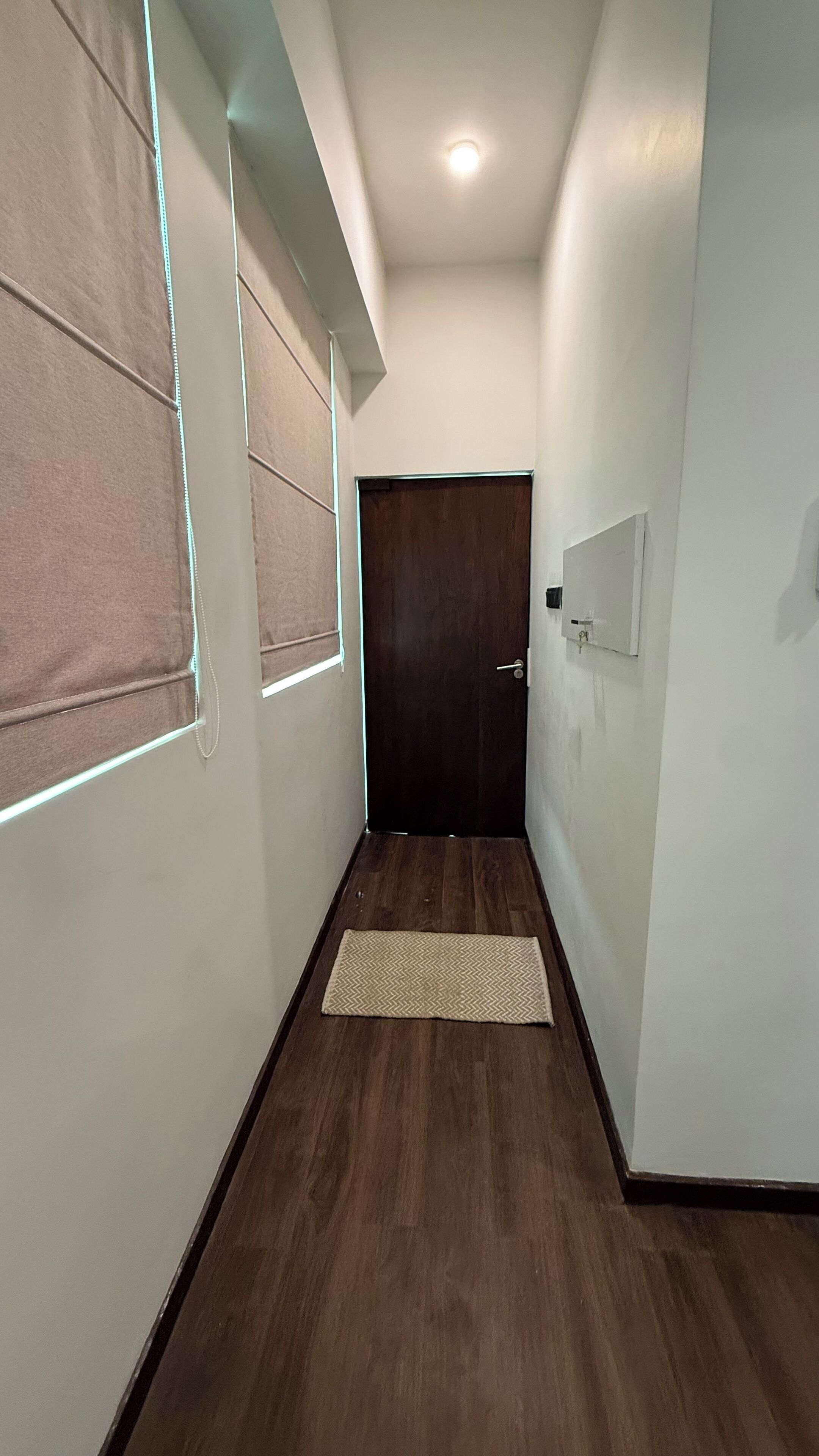 A hallway with a wooden floor, a dark door at the end, and a light switch on the wall.