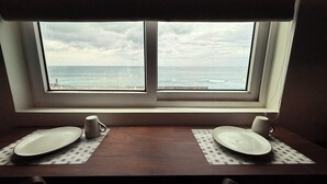 Ein Esstisch mit zwei Tellern und zwei Tassen vor einem Fenster mit Blick auf das Meer.