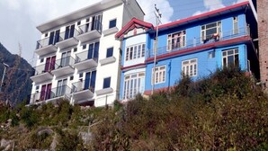 A multi-story building with balconies, a red roof, and a mountainous backdrop. - The Jungle Hut (Dharamshala)