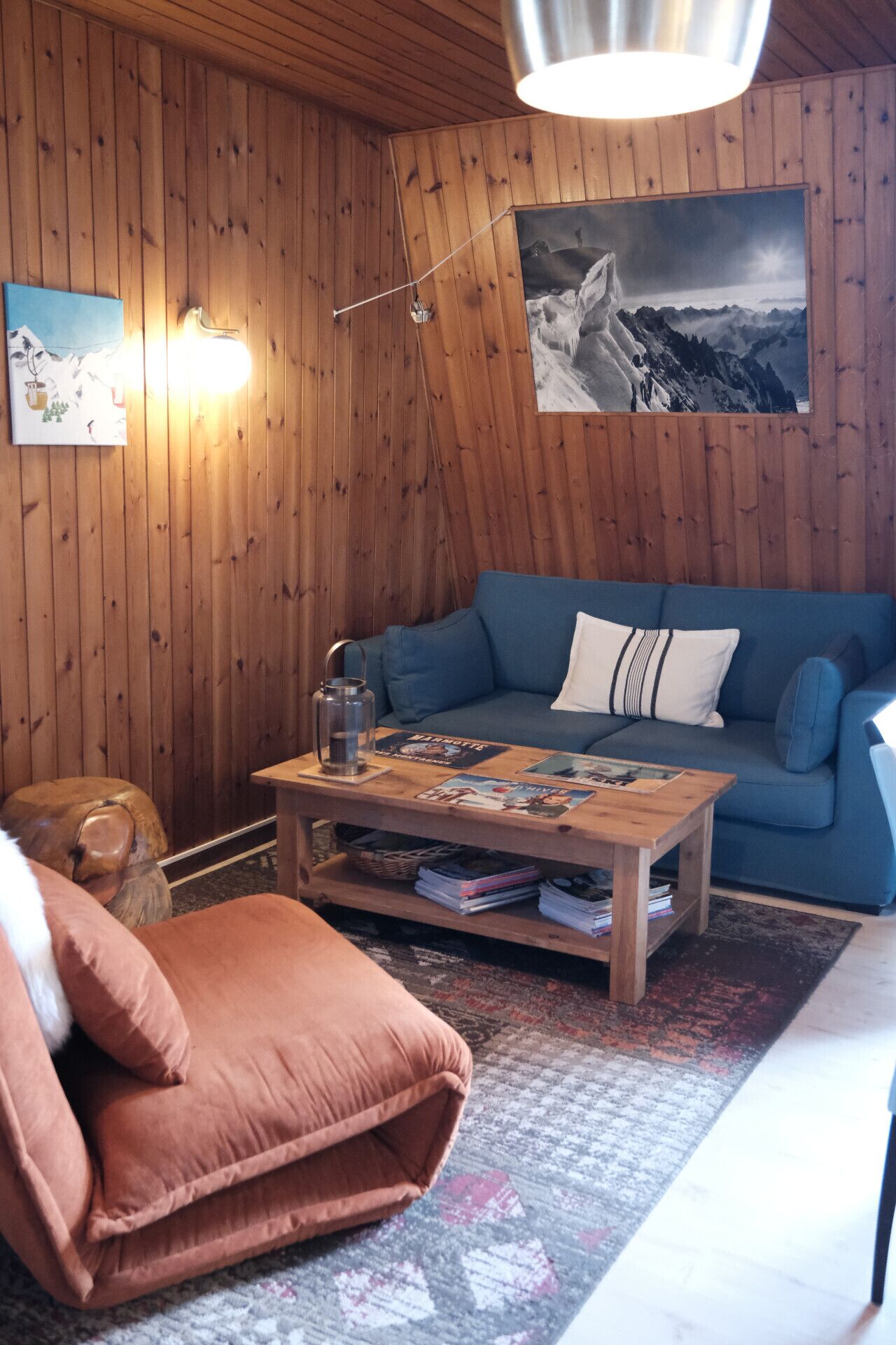 Ein gemütliches Zimmer mit Holzwänden, einem blauen Sofa, einem Holztisch mit Zeitschriften und einem großen gerahmten Bild an der Wand.