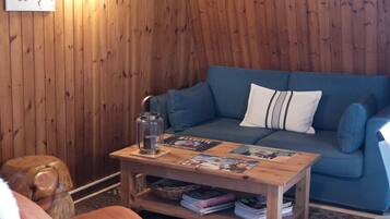Ein gemütliches Zimmer mit Holzwänden, einem blauen Sofa, einem Holztisch mit Zeitschriften und einem großen gerahmten Bild an der Wand.