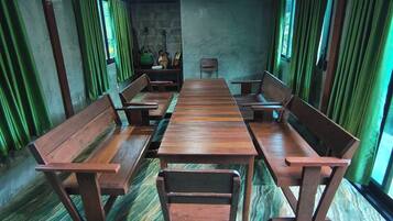 A room with a long wooden table and benches, green curtains, and a stone wall.