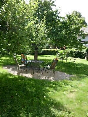 Eine Terrasse mit Tisch und Stühlen, umgeben von üppiger Bepflanzung und Bäumen.