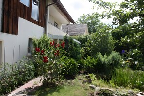 Ein modernes, zweistöckiges Haus mit Balkon, umgeben von einem Garten mit verschiedenen Pflanzen und einem kleinen Teich.