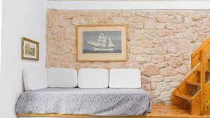 A stone wall, a framed picture of a sailboat, a sofa with cushions, and a wooden staircase. - Apartment in Aparthotel 'Unit 5' with Private Terrace, Wi-Fi and Air Conditioning (Αίγινα)