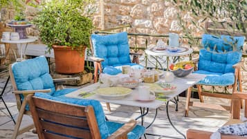 Een terras met blauwe fauteuils met kussens, een tafel met borden, bekers en een potplant.