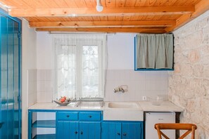Una cocina con armarios azules, un lavabo blanco y una pared de piedra.