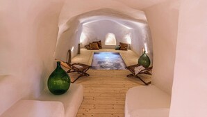 Una habitación abovedada e insulada con suelo de madera, una zona de estar central con cojines y dos jarrones verdes.