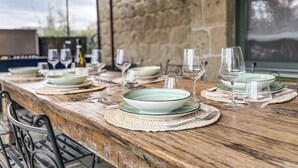 Una mesa de madera rústica dispuesta para comer, con platos verdes, vasos transparentes y cubiertos.