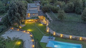 Una casa de dos pisos con piscina, rodeada por un jardín iluminado y un sendero de piedra.