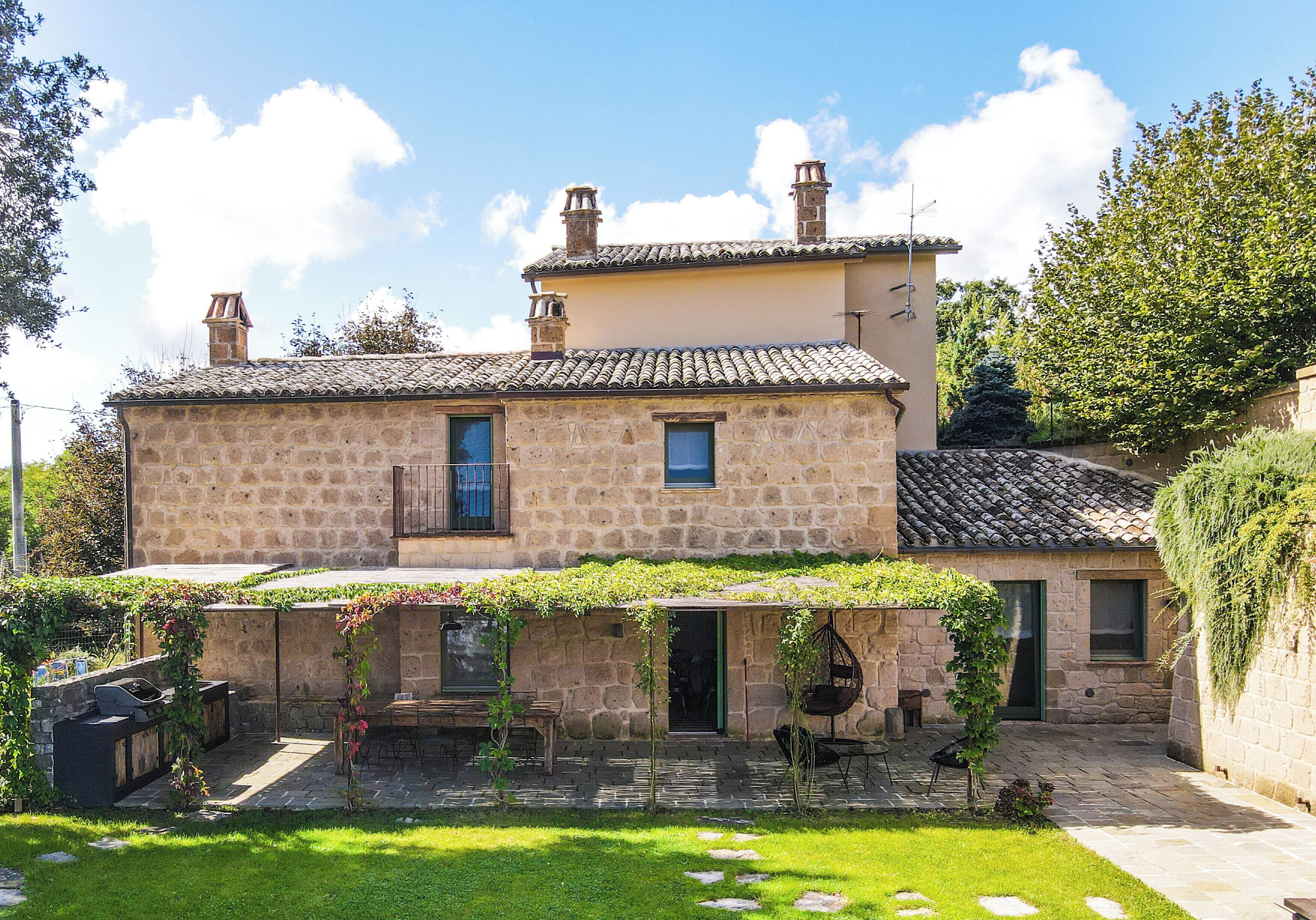 A stone house with a tiled roof, a covered patio, and a small garden.