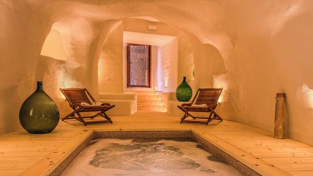 Un cuarto de spa con hidromasaje, piso de madera, dos camastros de madera y una pared de piedra.