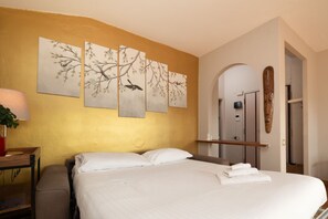 A hotel room with a bed, a nightstand, a lamp, and artwork on the wall.