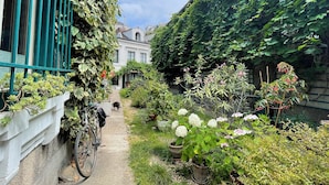 En smal passage med en cykel, plantekasser og en bygning med slyngplanter på muren.