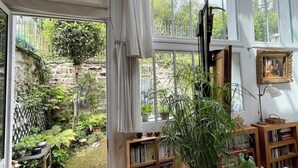 Et værelse med stort vindue, trægulv, bogreol og en potteplante.