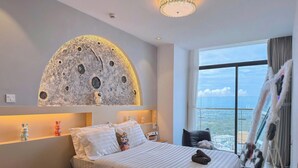 A modern hotel room with a large bed, a wall mural of the moon, a view of the city, and a balcony with a railing. - CSJ TOWER (Ho Chi Minh City)