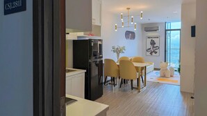 A modern kitchen with a black refrigerator, a dining area with yellow chairs, and a large window offering a city view. - CSJ TOWER (Ho Chi Minh City)