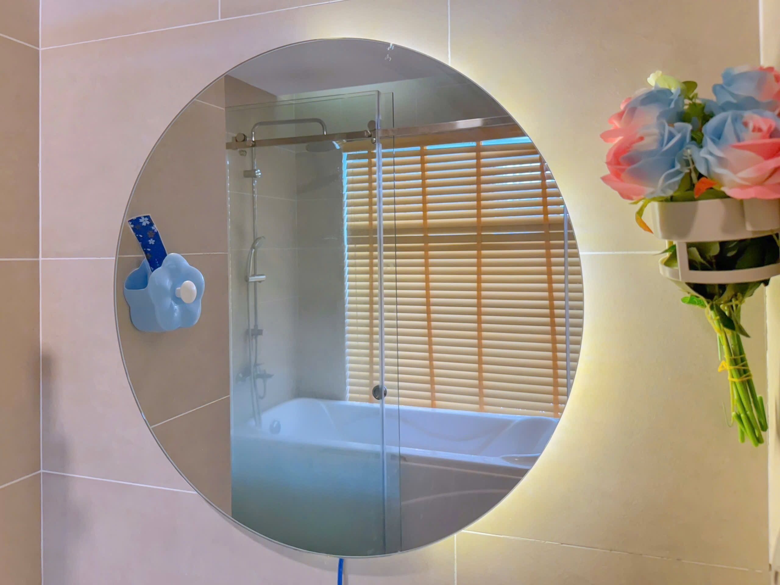 A bathroom with a round mirror, a shower, and a toilet.