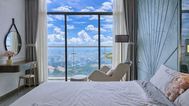 A modern hotel room with a large bed, a sitting area, a vanity with a mirror, and a view of the city through floor-to-ceiling windows. - CSJ TOWER (Ho Chi Minh City)