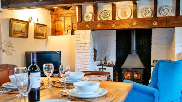Un comedor con una mesa de madera dispuesta para una comida, una silla azul y una chimenea con platos decorativos arriba.