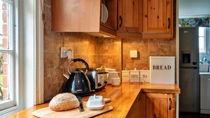 Una cocina con armarios de madera, una encimera, una caja de pan, un hervidor y una hogaza de pan sobre una tabla de cortar.