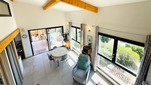 Een ruime kamer met een hoge plafond, houten balken, een eethoek met een tafel en stoelen, een bank en grote ramen met uitzicht op het omliggende landschap.