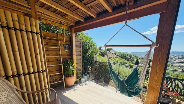 Een houten terras met rieten stoelen, een hangmat en potplanten.