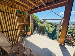 A wooden deck with wicker chairs, a hanging hammock, and potted plants. - House on a property with a swimming pool (Bormes-les-Mimosas)