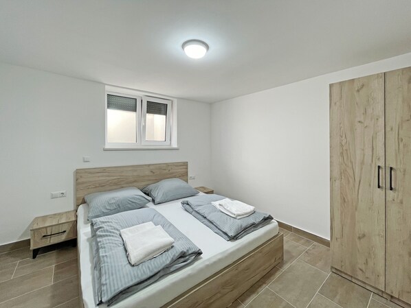Un dormitorio con cama, ventana, armario y mesita de noche.