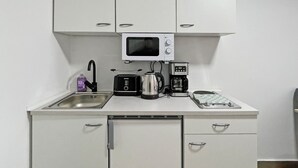 Una kitchenette compacta con microondas, tostadora, cafetera y un lavamanos pequeño.