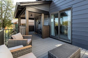 Et overdækket udendørsområde med fletmøbler, en træterrasse og en skydedør til en balkon.